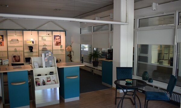 Moderner Optikerladen mit Empfangstresen, Beratungsecke, Prospekten und Brillenregalen.